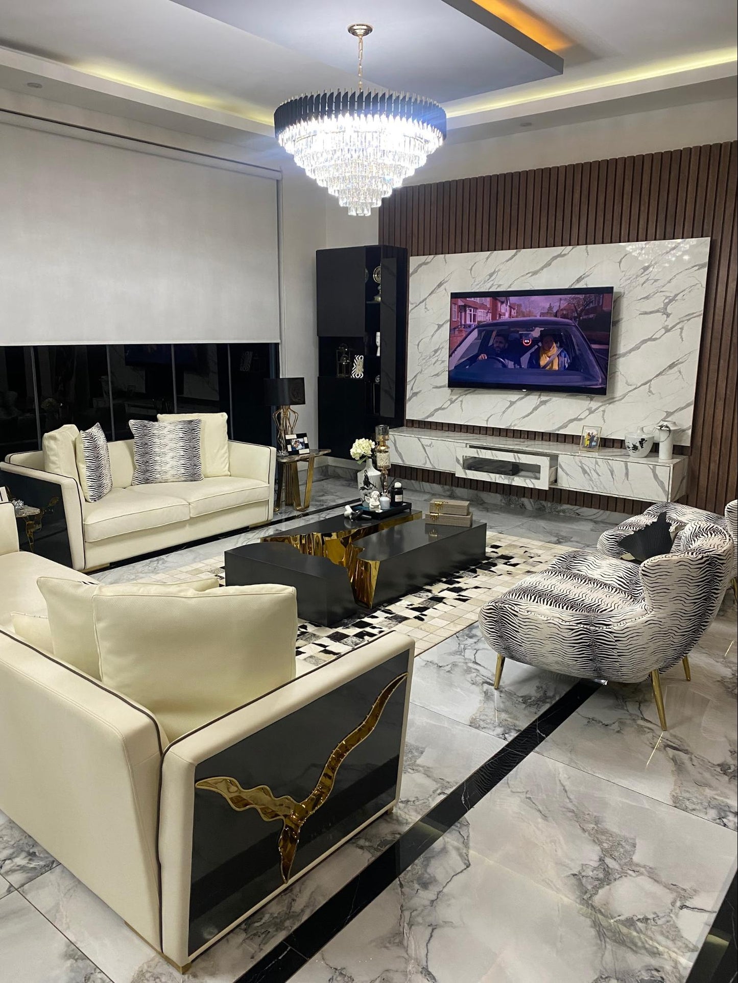 Luxury living room setup with marble tiles, featuring a sofa, cinema chairs, side tables, lamps, and a chandelier.